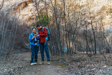 Two young hikers with backpacks navigating a forest trail using a smartphone gps app, searching for...
