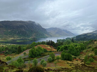 Fototapeta premium Stormy and rainy weather over Loch Shiel in the Scottish Highlands, with a cloudy sky, lush greenery and mountains surrounding the beautiful lake. Glenfinnan, Scotland, UK.