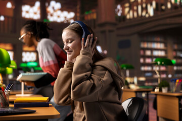 College student listening to ambient study music on headphones and focusing on her school projects, using a non traditional way to study and concentrate in the library. Girl enjoys focus music.