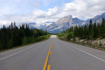 Empty road along the Saskatchewan River, Abraham Lake, and a lush forest with the snow-capped Rocky Mountains in the background