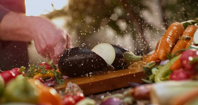 Close-up view of an expert chef cutting an eggplant with sharp knife on a rustic wooden board. Super slow-motion footage
