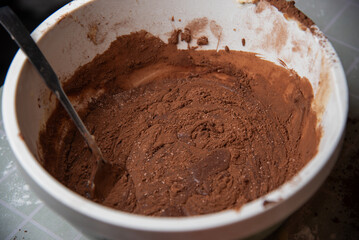 Close-up of chocolate cake batter in a mixing bowl with a spoon, rich texture and cocoa powder visible