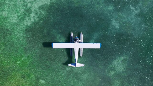 This aerial shot captures a seaplane docked on crystal-clear waters in Key West, Florida, as the camera ascends, revealing vibrant tropical colors and the scenic beauty of this coastal paradise.