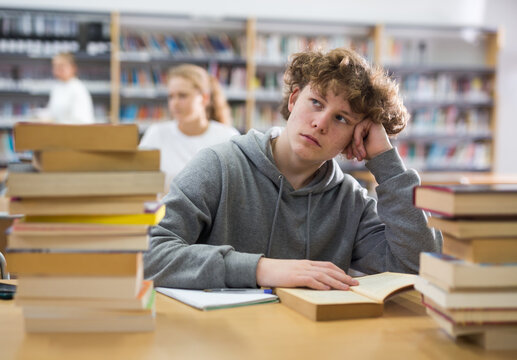Bored teenage boy trying to prepare for exam in school library