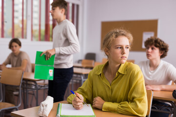 Obraz premium Focused teenage students studying in classroom with teacher, writing lectures in workbooks