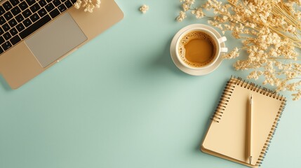 Warm cup of coffee beside a laptop, notebook, and dried flowers on a light blue workspace