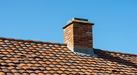 Naklejka premium Close-up of a brick chimney on a tiled roof against a clear blue sky
