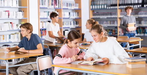 Two female friends reading books together and preparing for exams in the school library
