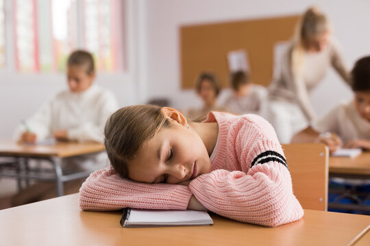 Portrait of tired school girl lying and sleeping at desk in classroom during lesson