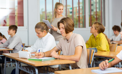 Group of diligent school kids and teacher during lesson in classroom in secondary school