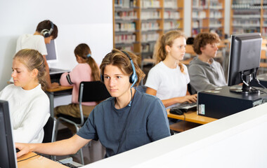 Group of young girls and boys sitting in computer classroom of library and exercising.