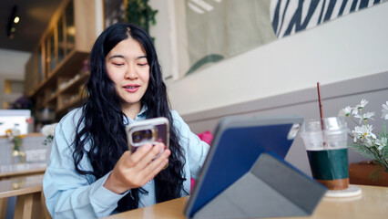 Fototapeta premium Businesswoman consultant motivation concept. Young woman using a smartphone and tablet in a cozy cafe setting.