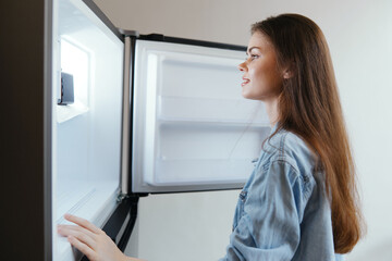 Young woman smiling while looking into an open fridge filled with fresh food, embodying healthy eating habits and a joyful lifestyle