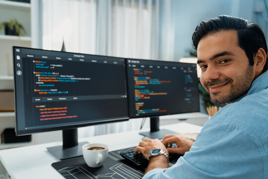 Smiling smart IT developer working software development looking camera with coding on two pc creating virus firmware application program version on website with coffee cup at modern office. Surmise.