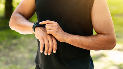 Closeup view of young guy checking his smartwatch or fitness tracker during training outdoors, panorama