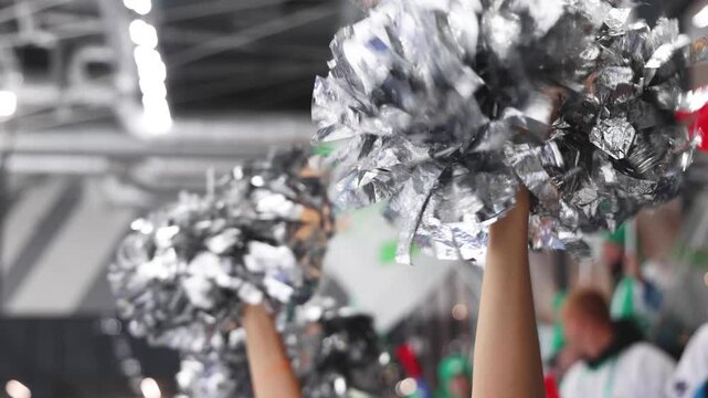 Female cheerleaders group in action, blue and white uniform with pom-pom, audience and hockey teams in the background, performing and supporting during ice hockey game match, cheerleading on ice arena
