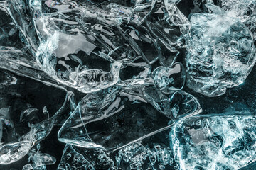 Pieces of crushed ice illuminated with blue light on black background. Abstract ice structure background, top view