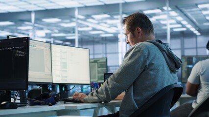 Fatigued admin stretching at work in server room to relieve muscle cramps while analyzing data on monitor. Tired man in data center relaxing body after overworking, camera A