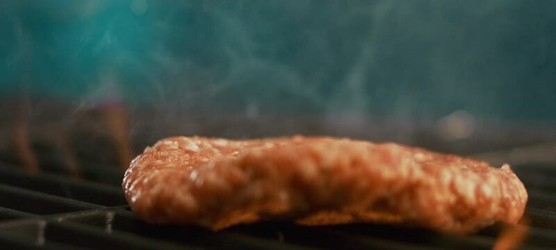 A raw piece of hamburger patty falling on an iron grill in slow-motion. Preparing meat for burger in the restaurant kitchen