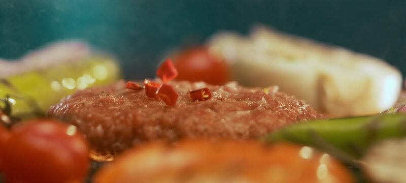 Fixed shot of red slice spices falling on hamburger patty in slow-motion