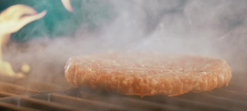 Juicy beef burger patty grilling on open fire at barbecue stove in super slow-motion