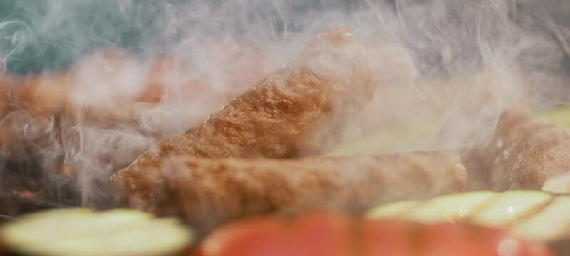 Ultra slow-motion shot of crispy cevapcici falling on heated pan in smoke background. Close-up view