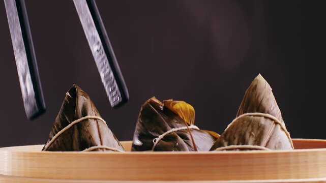 Hand holding zongzi (rice dumpling) with savoury fillings wrapped in bamboo or reed leaves.