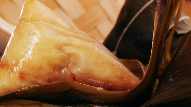 Hand holding zongzi (rice dumpling) with savoury fillings wrapped in bamboo or reed leaves.