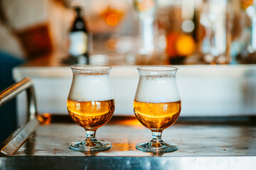 two glasses filled with foamy golden beer on metal surface.
