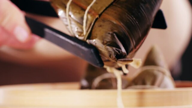 Hand holding zongzi (rice dumpling) with savoury fillings wrapped in bamboo or reed leaves.