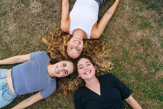Three smiling girls lying on grass forming a triangle with their heads