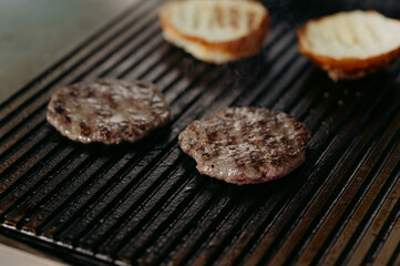 Sizzling burgers cooking on a grill with toasted buns nearby, perfect for a delicious meal. Capture the essence of outdoor grilling indoors with great flavor.