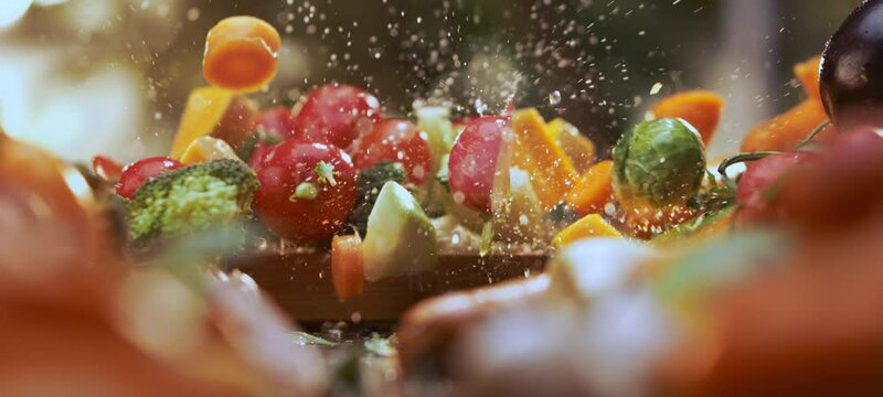 Super slow-motion shot of a male chef dropping mix sliced vegetables on wooden chopping board