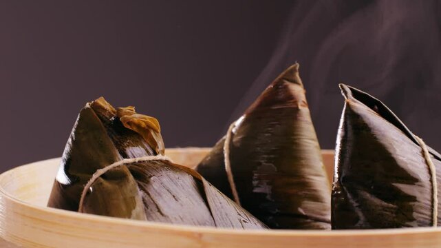 Hand holding zongzi (rice dumpling) with savoury fillings wrapped in bamboo or reed leaves.