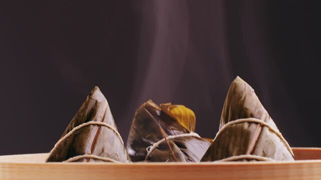 Hand holding zongzi (rice dumpling) with savoury fillings wrapped in bamboo or reed leaves.
