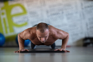 Fototapeta premium A muscular man performing push ups in the gym, showcasing strength, endurance, and dedication to his fitness routine.
