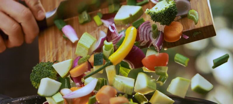 Close-up of male hands putting sliced mix vegetables in bowl, cooking salad at home in the kitchen. Nutrition and vegetarian diet concept