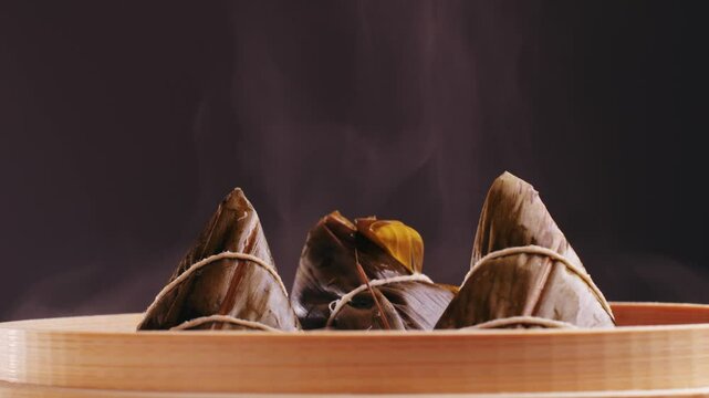Hand holding zongzi (rice dumpling) with savoury fillings wrapped in bamboo or reed leaves.