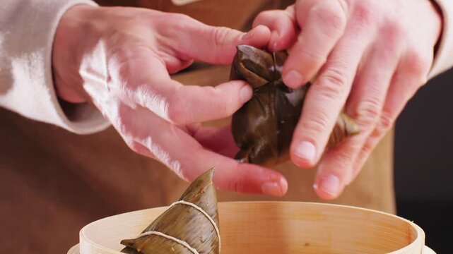 Hand holding zongzi (rice dumpling) with savoury fillings wrapped in bamboo or reed leaves.