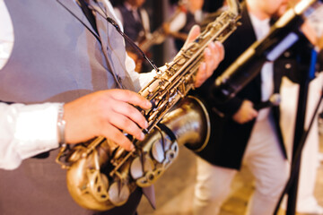 Concert view of saxophonist musician, saxophone sax player with vocalist and musical band during jazz orchestra show performing music on a stage in the scene lights, concert in a musical club hall