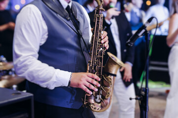 Fototapeta premium Concert view of saxophonist musician, saxophone sax player with vocalist and musical band during jazz orchestra show performing music on a stage in the scene lights, concert in a musical club hall