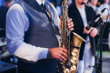Fototapeta premium Concert view of saxophonist musician, saxophone sax player with vocalist and musical band during jazz orchestra show performing music on a stage in the scene lights, concert in a musical club hall