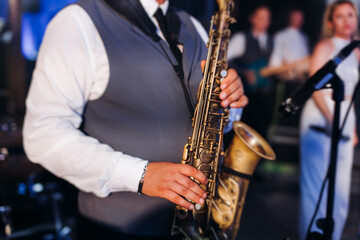 Fototapeta premium Concert view of saxophonist musician, saxophone sax player with vocalist and musical band during jazz orchestra show performing music on a stage in the scene lights, concert in a musical club hall