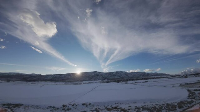 Aerial-FPV-Flying over snowy field in the shadow of sundown to the last glow of the setting sun as it disappears behind the mountain - High wispy clouds in a dark blue sky