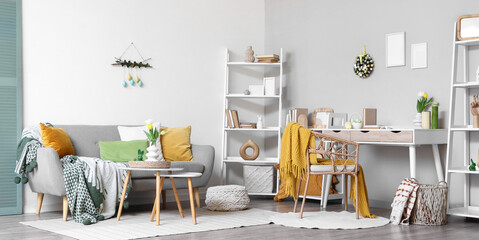 Interior of living room decorated for Easter with workplace, shelf units and sofa