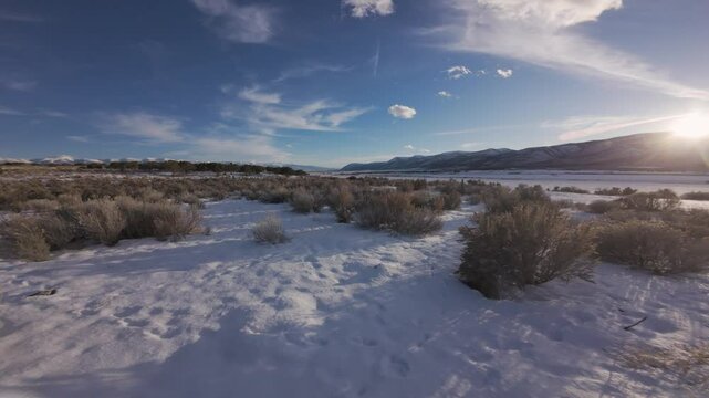 Aerial-FPV-First person view-Flying over pole fence-Low over snowy ground winding through tall sage with low shadows cast from setting sun