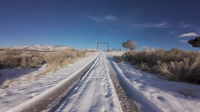 Aerial-FPV-First person view-Drone chasing its own shadow up snowy road and through gate under a blue sky 