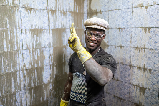 Bricklayer showing victory sign while tiling bathroom in Senegal