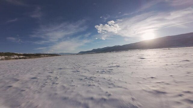 Aerial-First person view-FPV-Fast and low over snowy field at sundown under blue sky with high wispy clouds 
