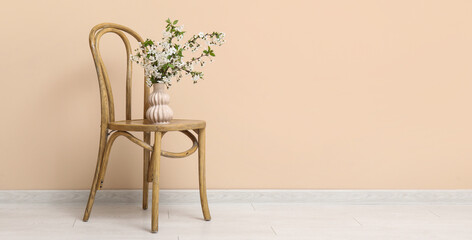 Fototapeta premium Blooming branches in vase on chair near beige wall